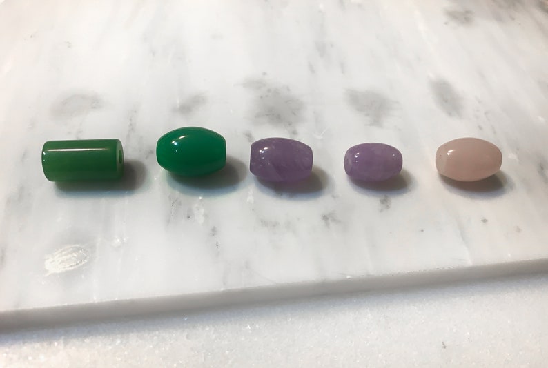 May include: Five oval-shaped gemstone beads. Two green jade beads, one purple amethyst bead, and two pink rose quartz beads.