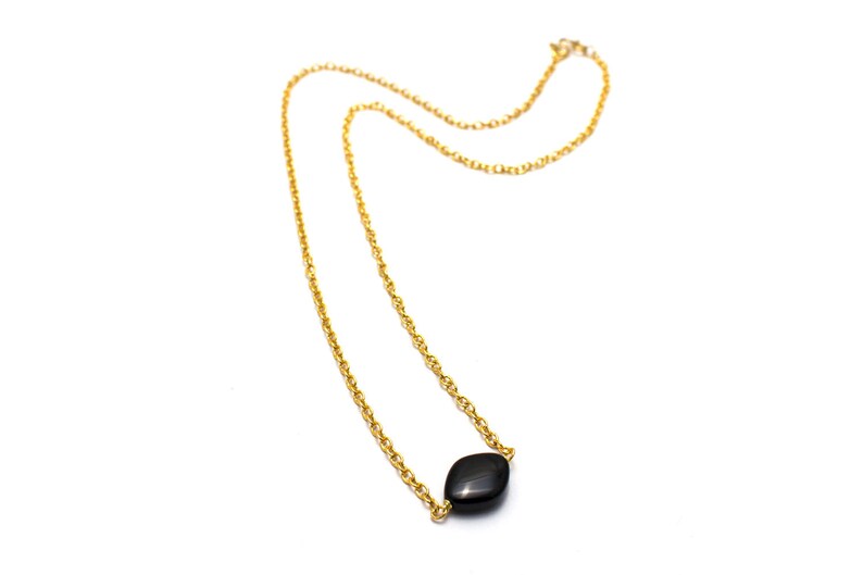 May include: A gold chain necklace with a single black gemstone pendant.