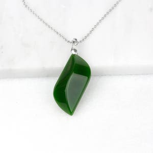 May include: A polished, dark green pendant necklace with a silver chain. The pendant is a smooth, teardrop shape. The necklace is displayed on a white marble surface.
