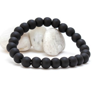 May include: A black beaded bracelet with a matte finish. The bracelet is made of round beads and is lying on a white surface.
