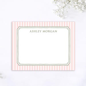 May include: A rectangular stationery card with a pink and white striped border. The card features a white interior with the name "ASHLEY MORGAN" in a simple font within a decorative frame.