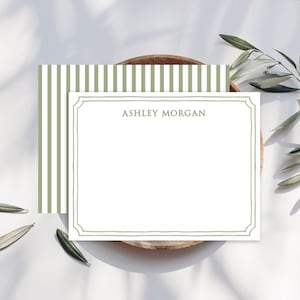 May include: White stationery with a sage green border and the name "ASHLEY MORGAN" printed in the center. The stationery is on a wooden tray with olive branches. The back of the stationery has vertical stripes in sage green and white.
