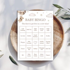 May include: Baby Bingo game card with a teddy bear and balloon graphic. The card features a grid with baby-related items like crib bedding, bath toys, and a high chair. The text reads "Baby Bingo" and "The first to get five in a row wins!"