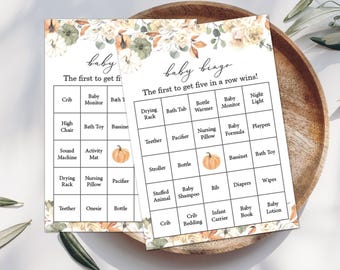 May include: Two baby bingo cards with a floral design. The cards have a grid of baby-related items like a crib, bottle, and pacifier. The text reads "baby bingo" and "The first to get five in a row wins!"