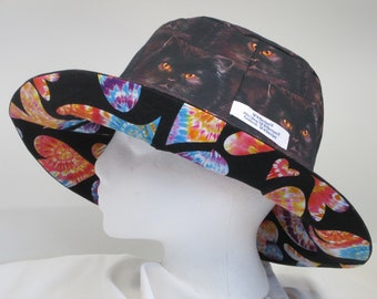 May include: A black wide-brimmed sun hat with a tie-dye pattern on the underside of the brim. The top of the hat features a black cat print with orange eyes. The hat has a label that reads "NEWFOUND" "HAND-MADE & DESIGNED" "PATTERNS BY NEWFOUND".