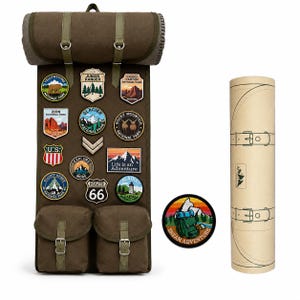 May include: A dark green canvas backpack with multiple patches from national parks and a Route 66 patch. The backpack has two front pockets and a roll-top closure. A cylindrical case and a patch with a backpack and the words "DREAM ADVENTURE" are also included.