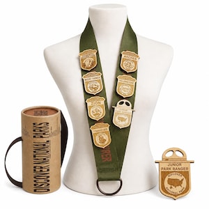 May include: A green lanyard with wooden Junior Park Ranger badges featuring national park names and logos. A cylindrical container with the text "DISCOVER NATIONAL PARKS" is on the left, and a separate wooden badge is on the right.
