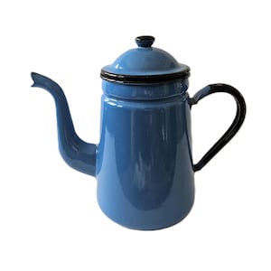 Puede incluir: Una taza de cerámica blanca con un asa negra y el texto "But First, Coffee" en negrita negra. La taza se encuentra sobre un fondo borroso, sugiriendo un ambiente acogedor.