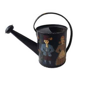 Könnte beinhalten: Schwarze Gießkanne aus Metall mit einem bemalten Design aus zwei Figuren in traditioneller Kleidung. Die Figuren sind ein Mann und eine Frau, beide mit lächelnden Gesichtern. Die Kanne hat einen Ausguss und einen Griff.