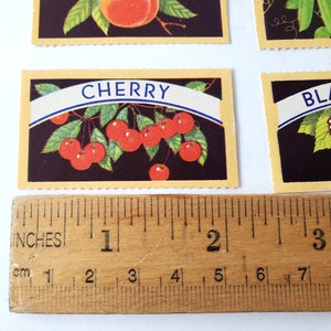 May include: A vintage card with a yellow border and a black background featuring a red cherry branch with the word "CHERRY" in a blue banner.