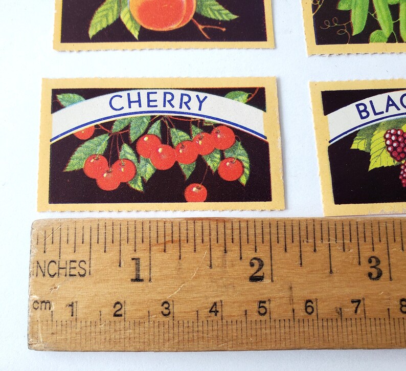 May include: A vintage card with a yellow border and a black background featuring a red cherry branch with the word "CHERRY" in a blue banner.