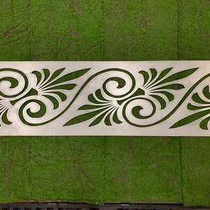May include: A rectangular silver-colored metal panel featuring a laser-cut pattern of repeating swirling scrolls and fan-shaped leaf motifs. The panel includes four small rectangular mounting slots, one located at each of the four corners.