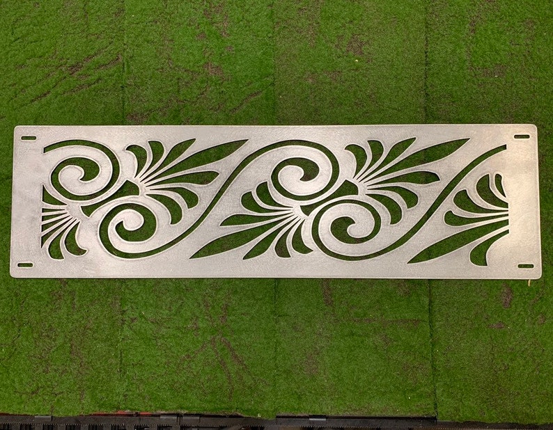 May include: A rectangular silver-colored metal panel featuring a laser-cut pattern of repeating swirling scrolls and fan-shaped leaf motifs. The panel includes four small rectangular mounting slots, one located at each of the four corners.