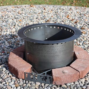 Metal fire ring insert placed in the center of one row of bricks and metal vent blocks. This image was taken as a still from the how to video included in the instructions. This set up helps to align the blocks and fire ring at the center of your patio although this is shown on a gravel patio.