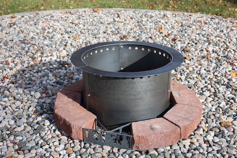 Metal fire ring insert placed in the center of one row of bricks and metal vent blocks. This image was taken as a still from the how to video included in the instructions. This set up helps to align the blocks and fire ring at the center of your patio although this is shown on a gravel patio.