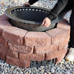 Image of a person inserting the assembled fire pit ring into the brick ring as part of the included insturctions and video on how to put it all together and create your own smokeless fire pit in your backyard in just one weekend.