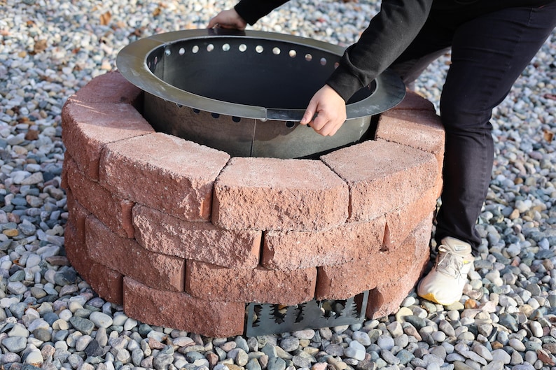 Image of a person inserting the assembled fire pit ring into the brick ring as part of the included insturctions and video on how to put it all together and create your own smokeless fire pit in your backyard in just one weekend.