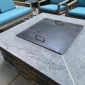 May include: A gray stone fire pit with a metal lid. The lid has two handles and is closed.