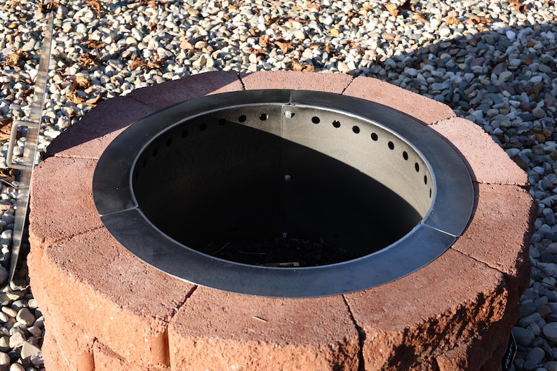 Fire ring insert with lid removed to see the vent holes at the top and bottom inside a brick fire pit ring.