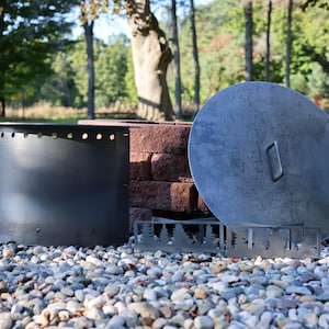Close-up of a DIY smokeless fire ring kit with pre-cut holes and welded lip, solid steel vent blocks, and solid lid with single handle in front of stacked retaining wall blocks on gravel patio.