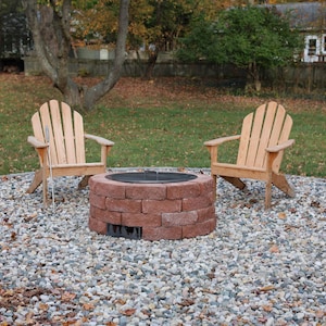Raw steel DIY smokeless fire pit kit with no fire and lid in place with two chairs in a back yard on a gravel patio.