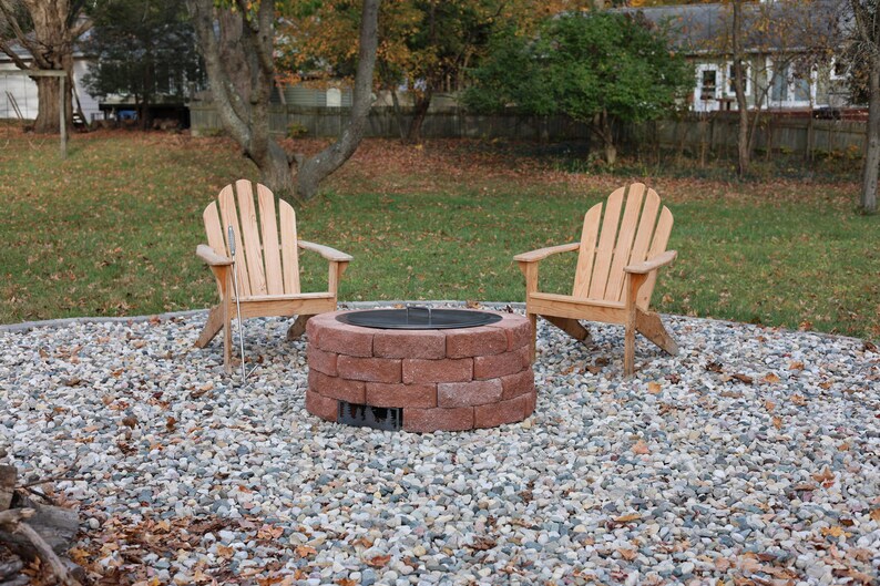 Raw steel DIY smokeless fire pit kit with no fire and lid in place with two chairs in a back yard on a gravel patio.