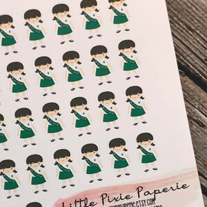 May include: A sheet of stickers featuring a repeated design of a girl scout in a green uniform with a sash. The stickers are on a white background and the text "Little Pixie Paperie" is at the bottom of the sheet.