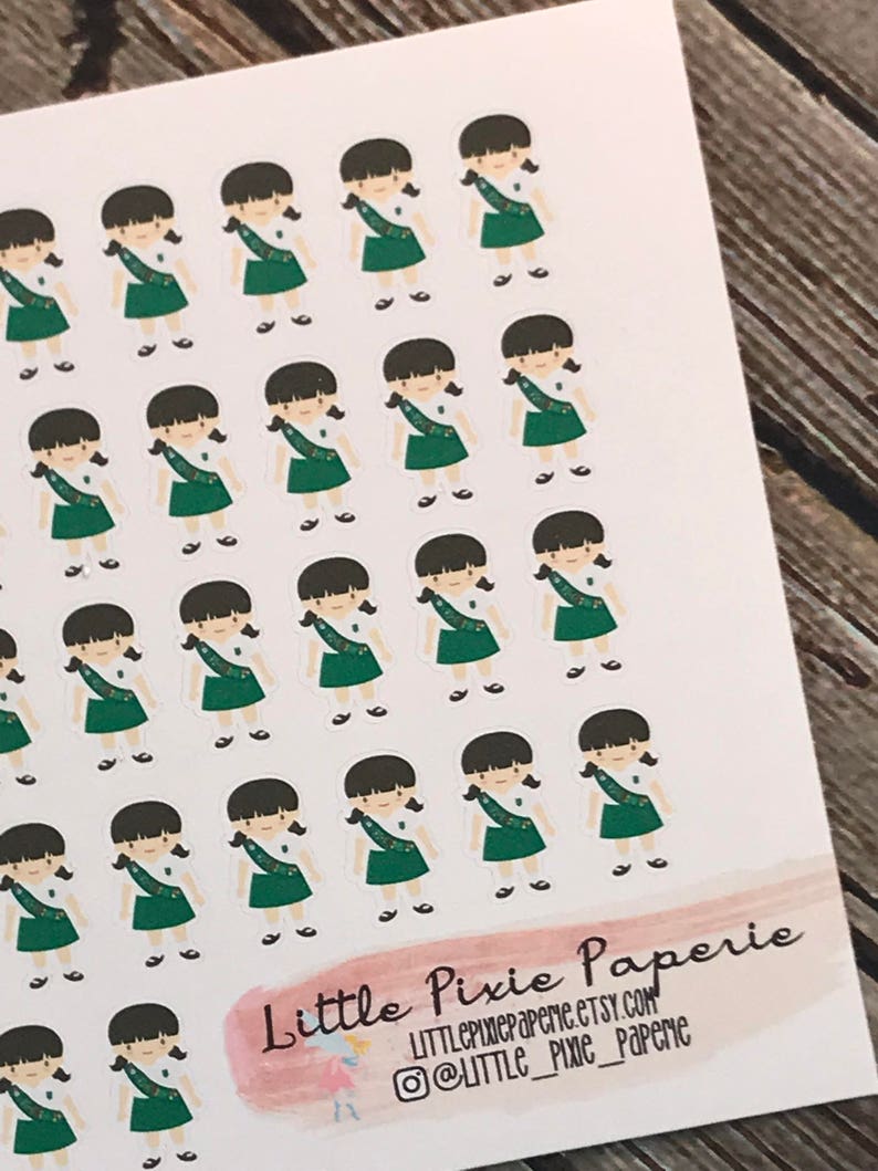 May include: A sheet of stickers featuring a repeated design of a girl scout in a green uniform with a sash. The stickers are on a white background and the text "Little Pixie Paperie" is at the bottom of the sheet.