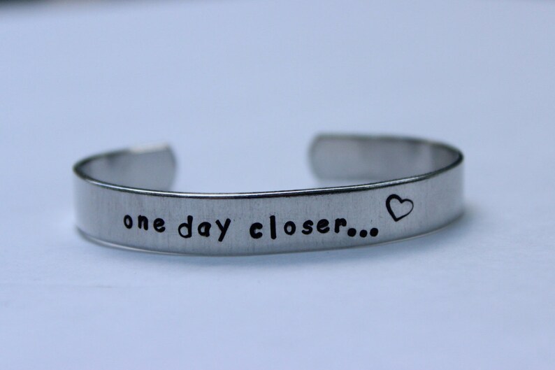 K&ouml;nnte beinhalten: Silberarmband mit der Aufschrift "one day closer..." und einem kleinen Herz.