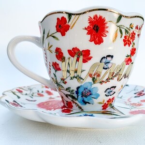 May include: White teacup and saucer with a floral pattern in shades of red, blue, and green. The teacup has a gold rim and the word "Mama" written in gold script.