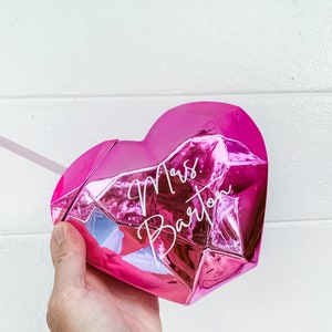 May include: Pink heart-shaped tumbler with a faceted design. The tumbler has the text "Mrs. Barton" written in white on the front.