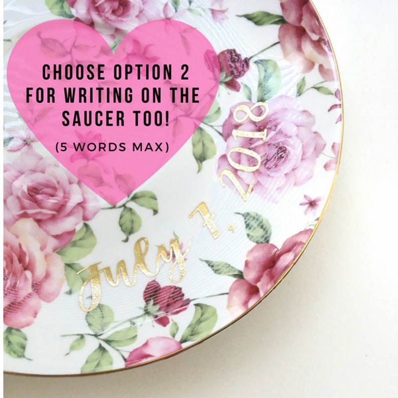 Puede incluir: Un plato de cer&aacute;mica blanco con un patr&oacute;n floral en tonos de rosa y verde. El plato tiene un borde dorado y presenta el texto "Choose option 2 for writing on the saucer too! (5 words max)" en un coraz&oacute;n rosa. La fecha "July 1, 2018" est&aacute; escrita en letras doradas.