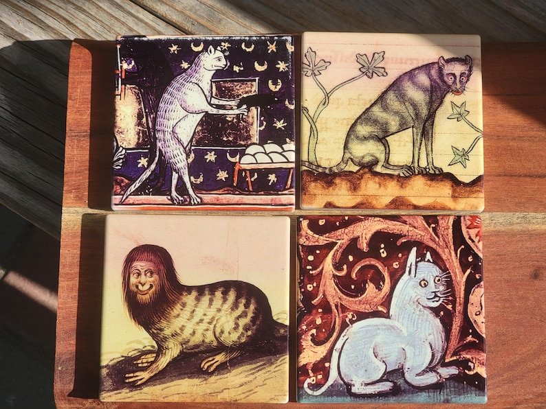 Puede incluir: Juego de cuatro posavasos cuadrados de cer&aacute;mica con ilustraciones de gatos de estilo medieval. Cada posavasos muestra un dise&ntilde;o de gato &uacute;nico en varias poses y entornos, con una est&eacute;tica vintage. Los posavasos est&aacute;n dispuestos sobre una superficie de madera.