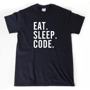 May include: Black t-shirt with the words "EAT. SLEEP. CODE." printed in white block letters. The shirt is a crew neck style and appears to be made of cotton. The text is centered on the front of the shirt.