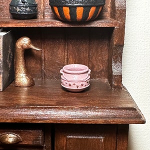 May include: A small pink cauldron with gold stars on the side, sitting on a wooden shelf.