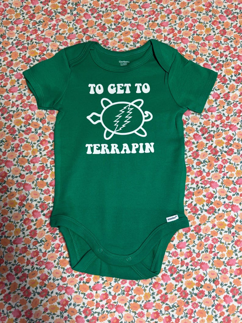 May include: Green baby onesie with the text "TO GET TO TERRAPIN" in white. A white turtle graphic with a lightning bolt design is centered below the text. The onesie is made of soft material and has short sleeves.