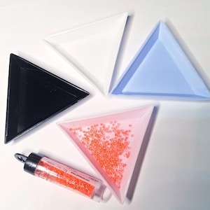 May include: Four triangular sorting trays in black, white, light blue, and light pink. The light pink tray contains small orange seed beads. A clear plastic tube with a black cap filled with matching orange seed beads is positioned below.