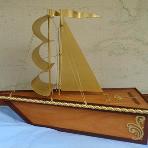 May include: A wooden model sailboat with gold sails and a gold rope trim. The sailboat has a small wooden box with a gold latch on the deck.