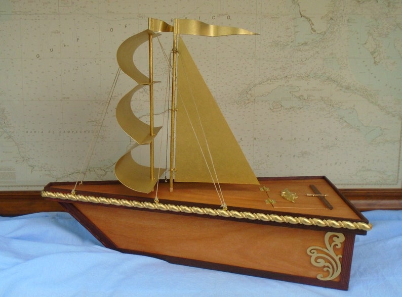 May include: A wooden model sailboat with gold sails and a gold rope trim. The sailboat has a small wooden box with a gold latch on the deck.