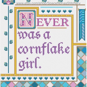 Puede incluir: Diseño de punto de cruz con el texto "NEVER was a cornflake girl." El diseño presenta un borde decorativo con detalles en azul, rosa y amarillo. La URL de la tienda Etsy es visible en la parte superior.