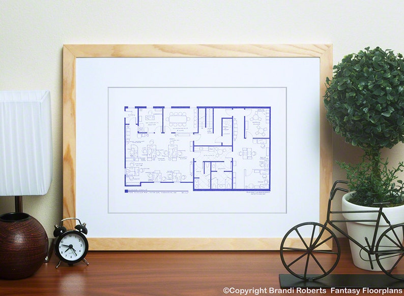 May include: A framed blueprint of an office floor plan. The plan is drawn in blue lines on a white background. The plan shows the layout of the office, including the location of desks, chairs, and other furniture. The plan is framed in a light wood frame.