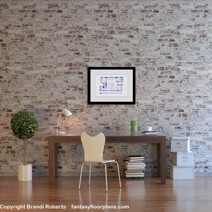 May include: A white desk chair with a curved back and a white desk with a framed blueprint hanging on a white brick wall. There are books stacked on the desk and a potted plant and a lamp on the desk.