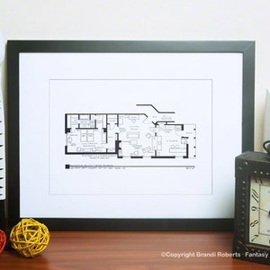 May include: Black and white floor plan print of a home with multiple rooms, including a living room, kitchen, and bedrooms. The print is framed in a black frame and is hanging on a wall.
