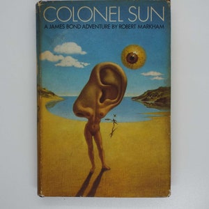 May include: A vintage paperback book cover with a surreal illustration of a woman with a giant ear for a head standing on a beach. The book title is "Colonel Sun" and the subtitle is "A James Bond Adventure by Robert Markham".