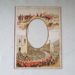 May include: A vintage photo frame with a round oval opening for a portrait. The frame features a colorful illustration of soldiers marching in a parade, with a scene of soldiers on horseback in the top portion. The text "1st. Dvn. Soudon 1885" is printed in the upper right corner. The bottom of the frame includes the text "The Troops of the New Soudan Soudan Routing Army" and "Sydney"