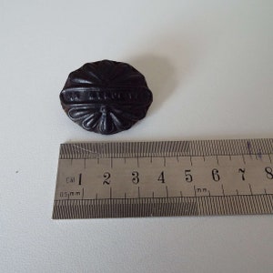 May include: A black rubber stamp with the words "UK Kingdom" embossed on it. The stamp is approximately 5 cm in diameter and has a floral design around the edge.