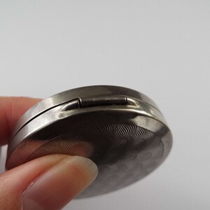 May include: A silver compact with a textured lid and a hinged closure.