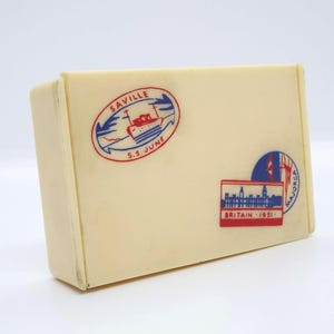 May include: A rectangular, off-white box with three colorful decals. One decal reads "SAVILLE S.S. JUNE" with a ship illustration. Another says "BRITAIN 1951" with a building illustration. The third says "MAJORCA".