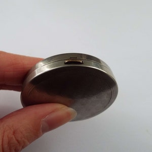 May include: A silver compact with a textured, circular design and a gold latch.