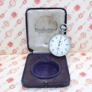 Puede incluir: Un reloj de bolsillo Venner Time Switches vintage con esfera blanca, números negros y caja plateada. El reloj se exhibe en su estuche original forrado de terciopelo negro y azul. El estuche está abierto, revelando el reloj y el nombre de la marca.
